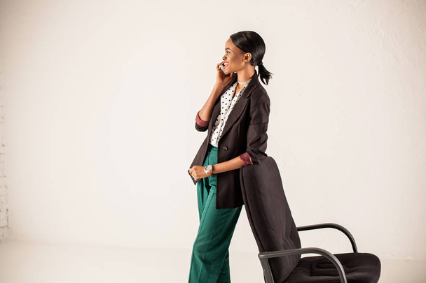 African american woman standing on a white background and leaning on an office armchair. - Fotografie, Obrázek