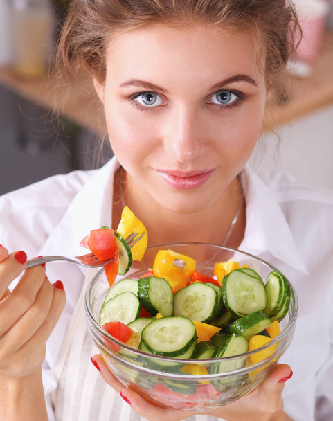 Mujer joven comiendo ensalada fresca en la cocina moderna - Foto, Imagen