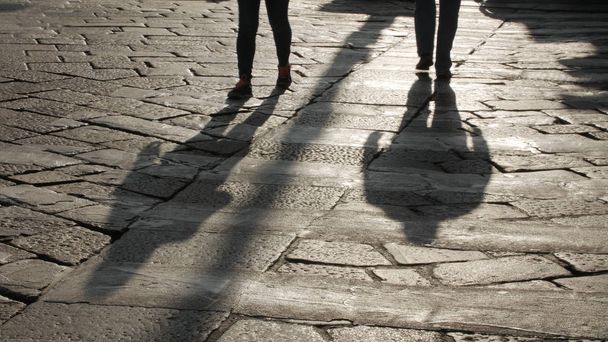 Silhouettes of people on the cobblestone pavement. - Фото, зображення