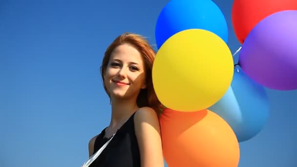 roodharige meisje met kleur ballonnen bij blauwe hemelachtergrond. - Video