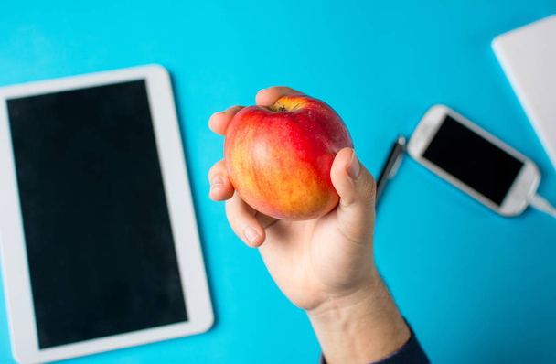 Χέρι κρατάει ένα μήλο με tablet και κινητό τηλέφωνο - Φωτογραφία, εικόνα