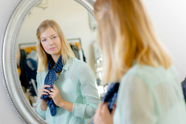 Lady trying on scarf, looking at reflection in mirror - Фото, зображення