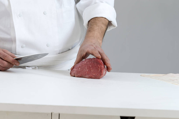 Closeup of the hands of a butcher cutting slices of raw meat off a large loin for tournedos - Photo, Image