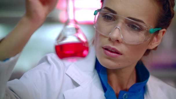 Female chemist in lab. Woman chemist analyzing chemical liquid in lab flask - Metraje, vídeo