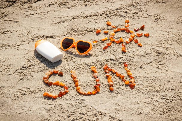 Word and shape of sun, sunglasses with sun lotion on sand at beach, summer time - Valokuva, kuva