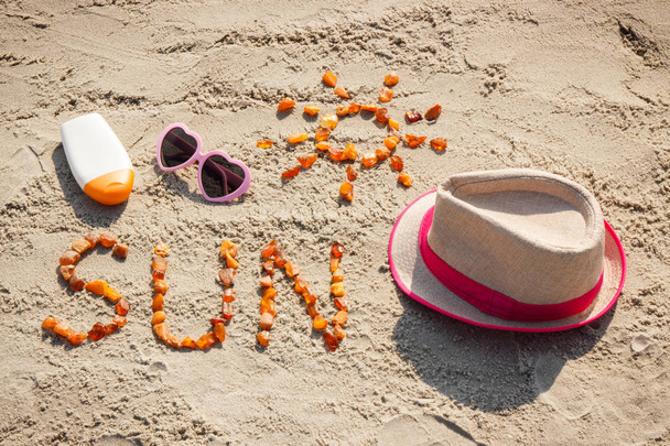 Слово і форма сонця, сонцезахисні окуляри, сонячний лосьйон і солом'яний капелюх на піску на пляжі, літній час
 - Фото, зображення