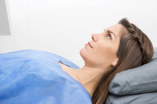 Женщина в защитной одежде лежит на больничной койке
 - Фото, изображение