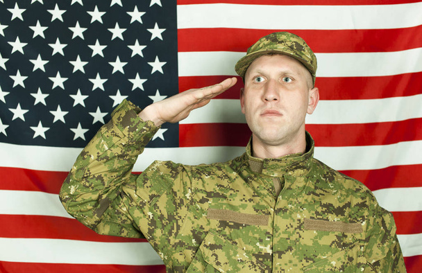 Serios junger Soldat salutiert gegen die amerikanische Flagge. Porträt  - Foto, Bild