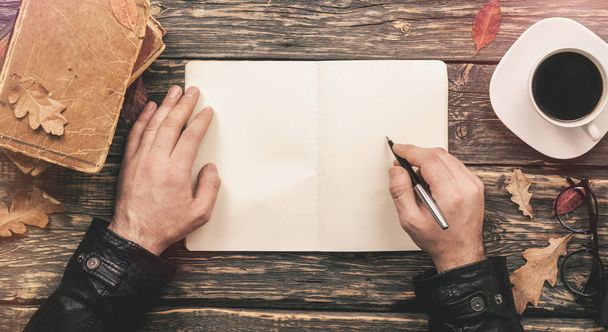 Male hand writing in a notebook on a wooden table - Photo, Image