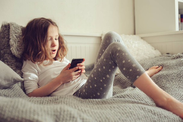 kid girl playing smartphone at home on the bed - 写真・画像