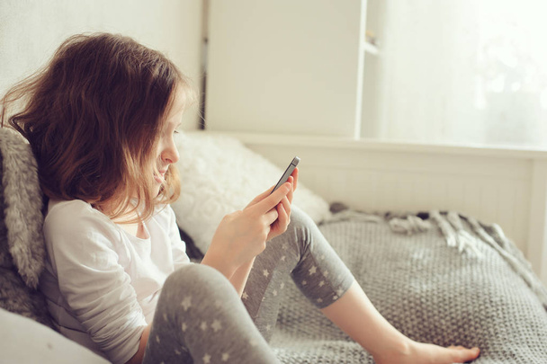kid girl playing smartphone at home on the bed - Foto, Bild