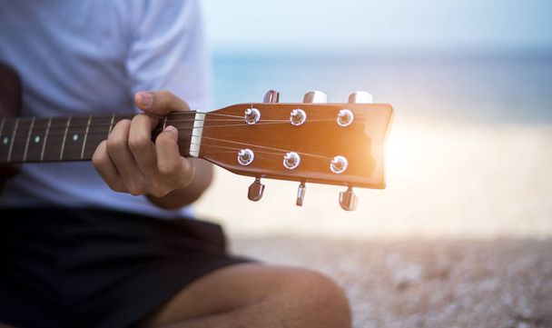 Close up handsome man playing classic guitar sitting on the beach in vacation - Foto, Imagen