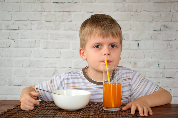 Cute little boy drinking carrot juice from straw on breakfast - Photo, Image