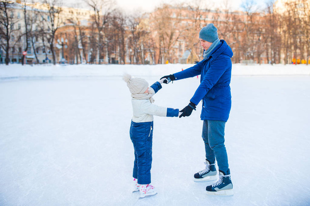 junger Vater und entzückendes kleines Mädchen haben Spaß auf der Eisbahn im Freien - Foto, Bild