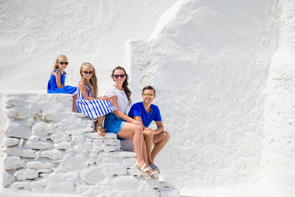 Семейный отдых в Европе. Родители и дети, сидящие на лестнице Парапортианской церкви на острове Миконос, Греция - Фото, изображение