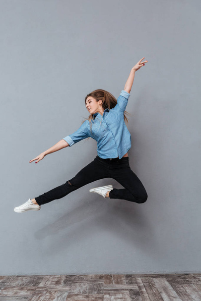 Full length portrait of woman in shirt jumping in studio - Φωτογραφία, εικόνα