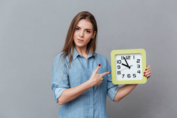 Серйозна жінка в сорочці тримає годинник
 - Фото, зображення