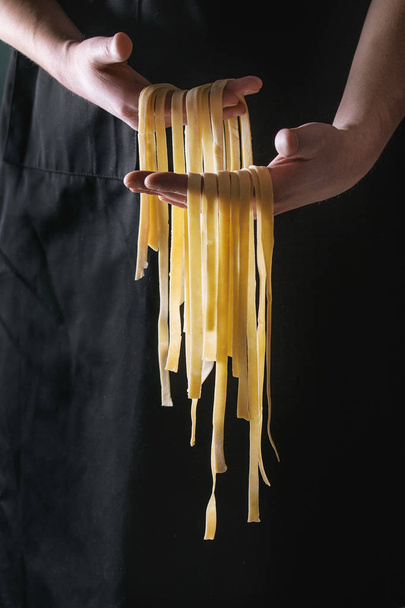 Fresh pasta tagliatelle in man's hands - Foto, afbeelding