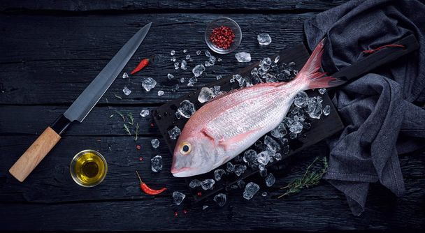 Ψάρια φρέσκα Ισπανικά τσιπούρα (breca) στον πάγο σε ένα μαύρο ξύλινο τραπέζι  - Φωτογραφία, εικόνα