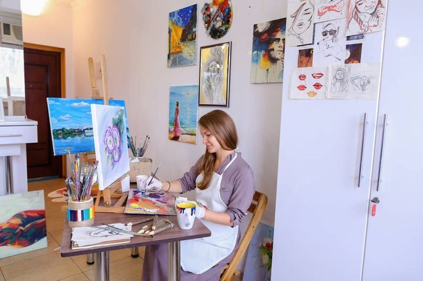 Dívka sedí na stoličce na stojan a psaní malba, používá štětec - Fotografie, Obrázek