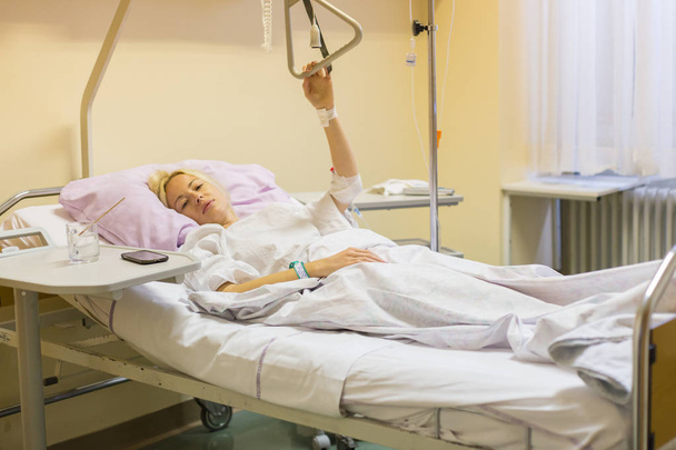 Paciente mujer postrada en cama recuperándose después de la cirugía en atención hospitalaria
. - Foto, imagen