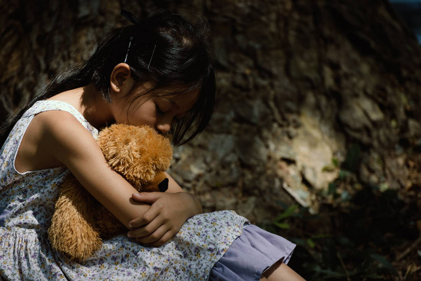 Adorable sad girl with teddy bear in park, Little girl is huggin - Photo, Image