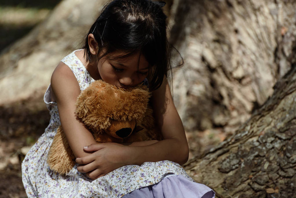 Adorable sad girl with teddy bear in park, Little girl is huggin - Photo, Image