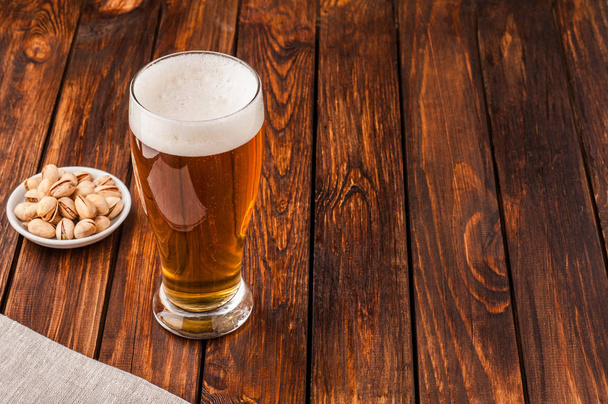 glass of light cold frothy beer, nuts old wooden table - Photo, image
