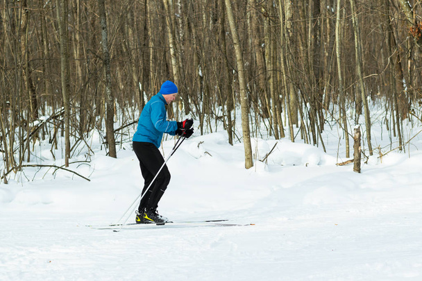 Un homme en costume bleu court sur des skis dans les bois d'hiver
. - Photo, image