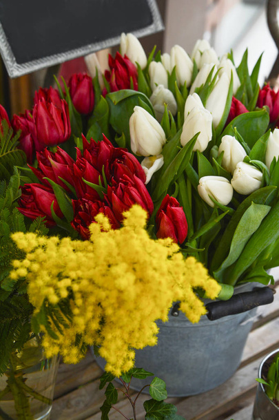 Frühlingsblumen - rote und weiße Tulpen und Mimosen auf einem Markt - Foto, Bild