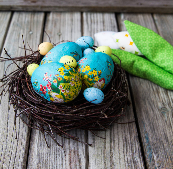 gekleurde eieren liggen in een nest op een grijze houten achtergrond - Foto, afbeelding
