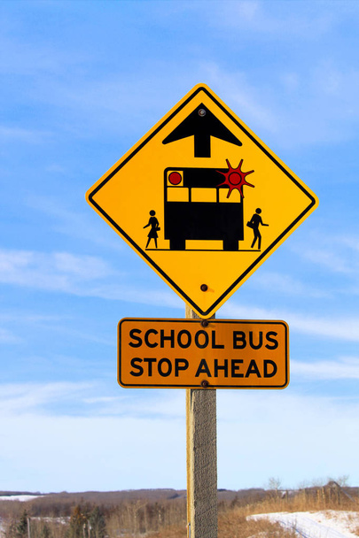 Primer plano de una parada de autobús escolar frente a un cartel contra un cielo azul
 - Foto, Imagen