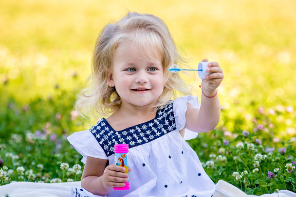 Little girls blow bubbles sitting on the grass - Photo, Image