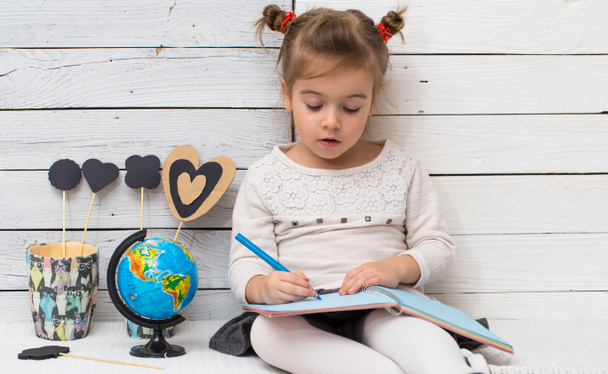 school girl sits on a white wooden background with a globe in his hands and a notebook - Foto, Bild