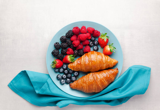 Summer breakfast of fresh wild berries and hot croissants - Фото, изображение