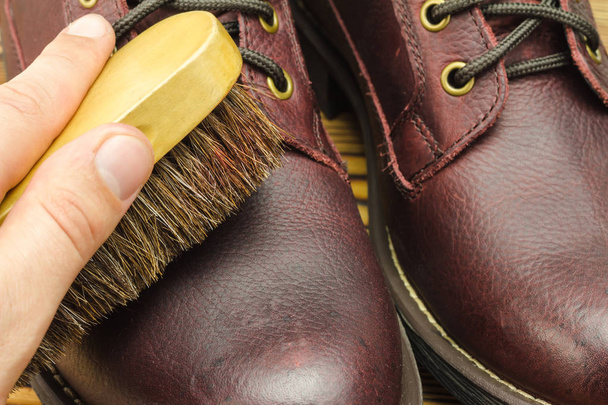 Main avec brosse, soin des bottes en cuir marron propre et polissage, vue rapprochée
 - Photo, image