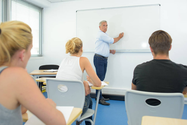 Profesor escribiendo en pizarra blanca delante de la clase
 - Foto, Imagen