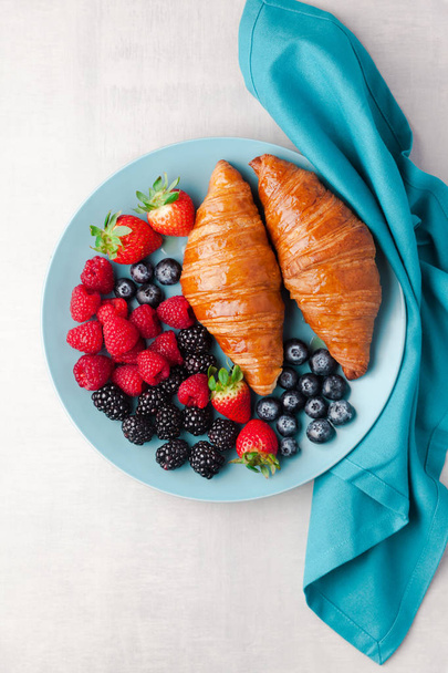 mixed berries and croissants on a blue plate on a white backgrou - Foto, Imagem