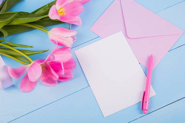 Bouquet of tender pink tulips with empty paper on blue wooden ba - Foto, Imagen