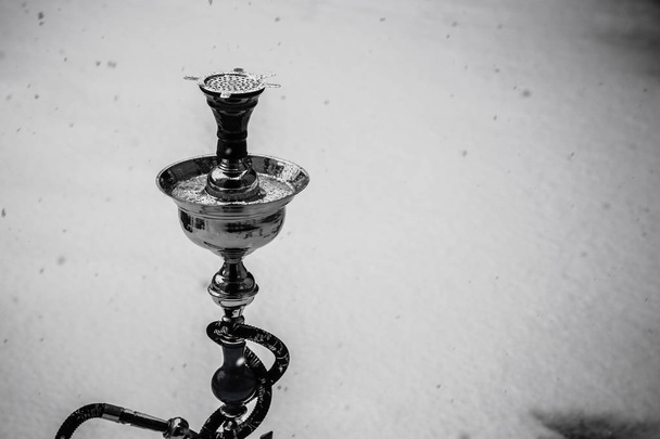 Μεγάλο ναργιλές καπνού Κατασκευασμένο από μέταλλο, γυαλί και κεραμικά. Χιονίζει. Χιόνι με φόντο. Λευκό - Φωτογραφία, εικόνα