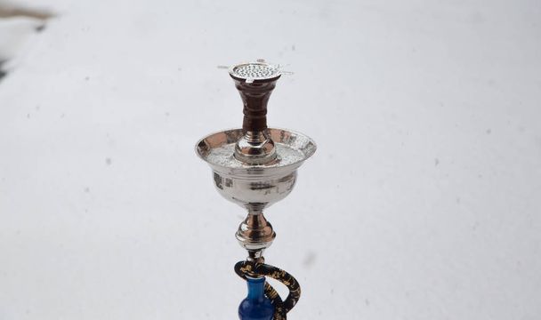 Iso vesipiippu metallista, lasista ja keramiikasta valmistetulle tupakalle. Sataa lunta. Lumen tausta. Valkoinen
 - Valokuva, kuva