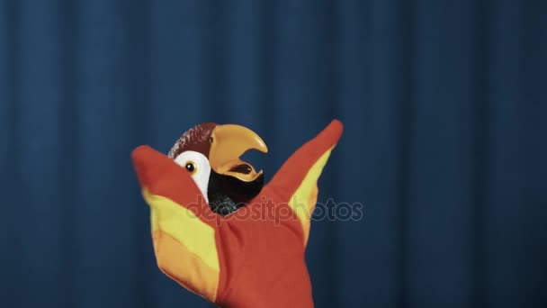 Hand puppet wrijven papegaai en verspreiden van wapens breed, zwaaien op blauwe achtergrond - Video