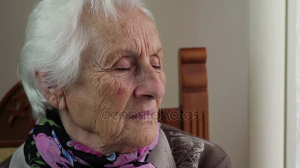  sad and pensive old woman sitting near the window - Felvétel, videó