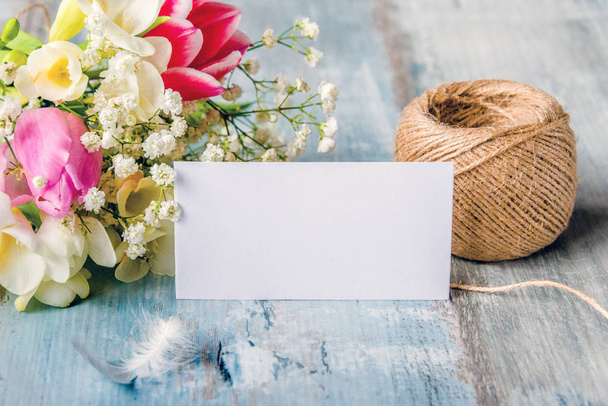 Empty greeting card. Spring flowers and feather over blue rustic wood background.  - Photo, Image