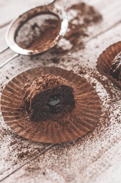 Chocolate Chip Muffin in braunem Wachspapier. ausgepackt. Kakaopulver im Hintergrund - Foto, Bild