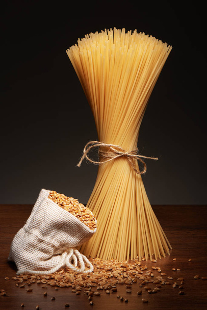 Dry spaghetti pasta and burlap bag of wheat grains  - Fotó, kép