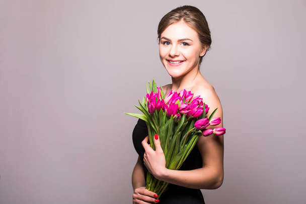 Beautiful girl with flowers tulips in hands on a light background - Фото, зображення