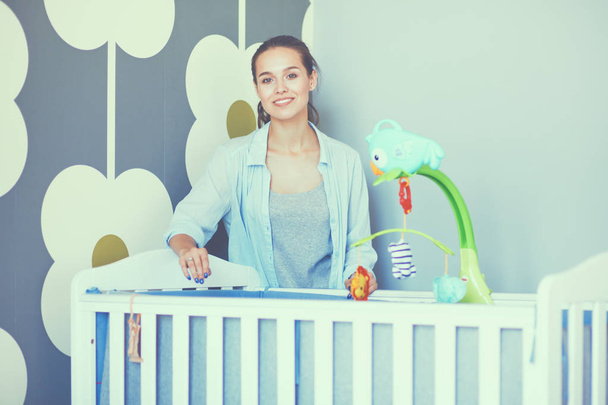 Young beautiful woman standing near children cot - 写真・画像