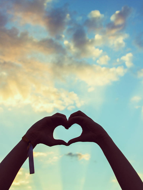 Καρδιά σχήμα από χέρια, νεαρή γυναίκα με ένα όμορφο ουρανό ως φόντο - Φωτογραφία, εικόνα