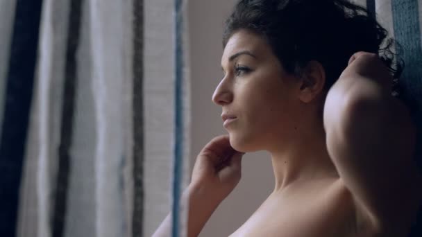 nachdenklich, junge Brünette berührt ihre Haare am Fenster - Filmmaterial, Video
